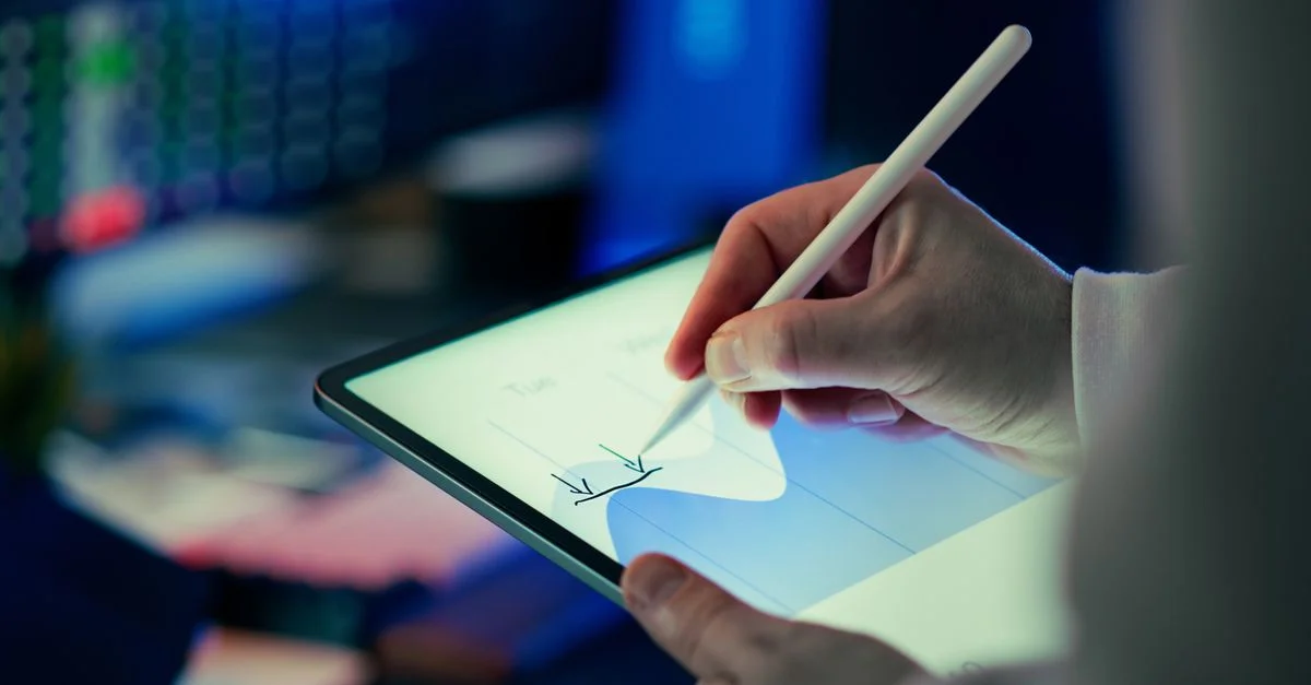 Un professionnel utilise un stylet pour analyser des données sur une tablette numérique dans un environnement de bureau.